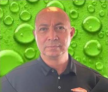 Male employee in dark shirt in front of green background. 